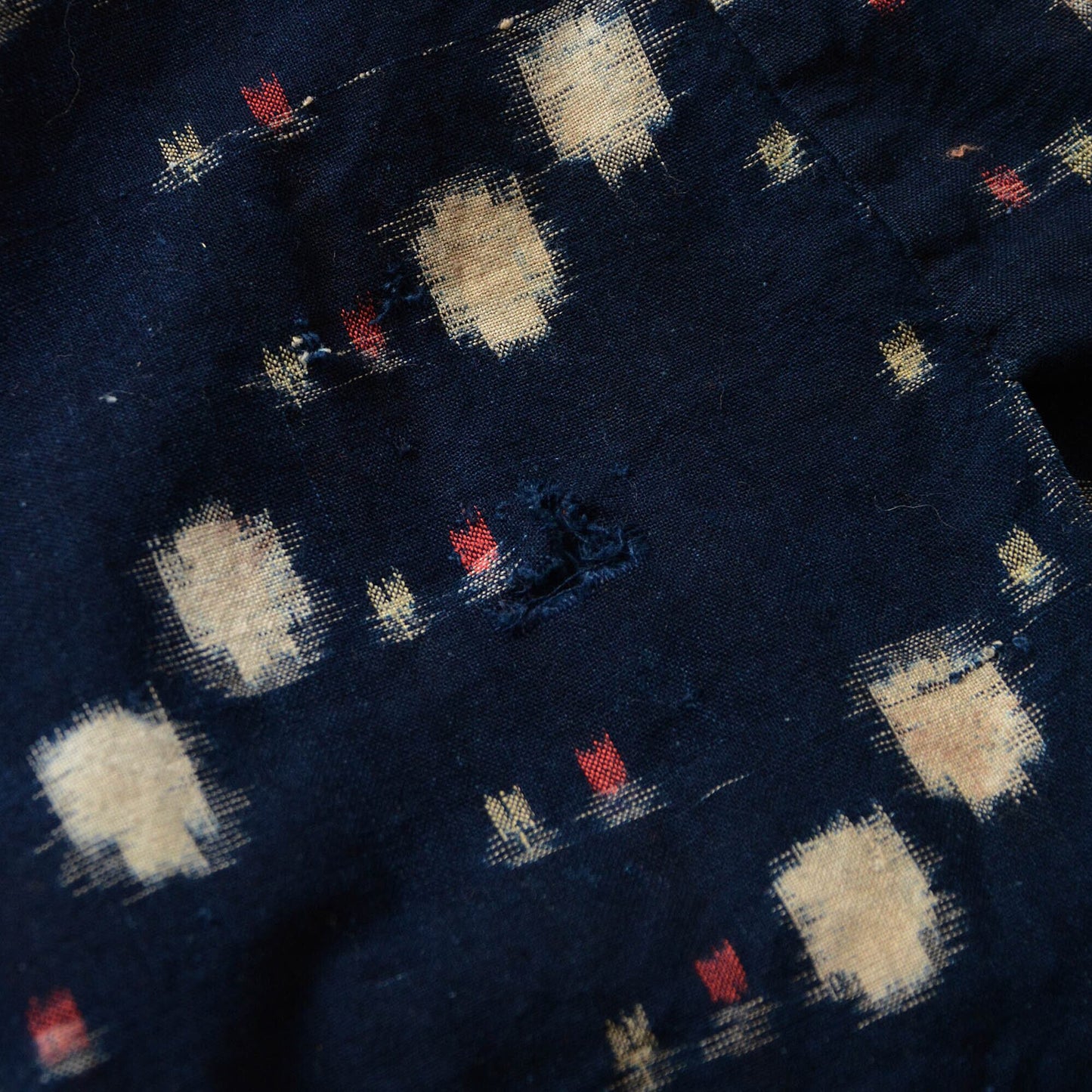 Close-up of a hole in an indigo kasuri noragi, highlighting its vintage wear and character