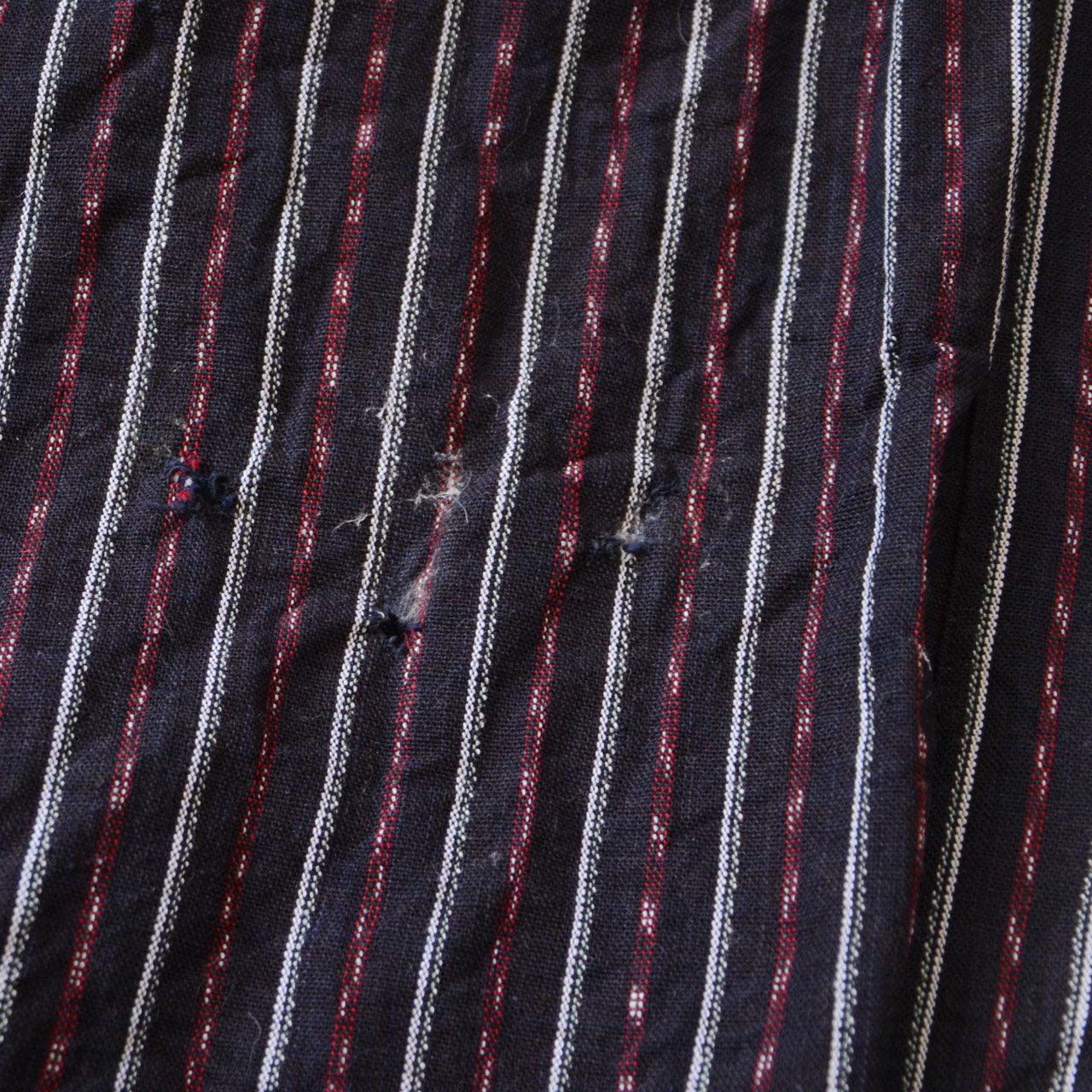 Close-up of the small holes on vintage Japanese monpe pants made from striped cotton fabric. These unique details can be creatively repaired with patching, adding character and charm to the pants.