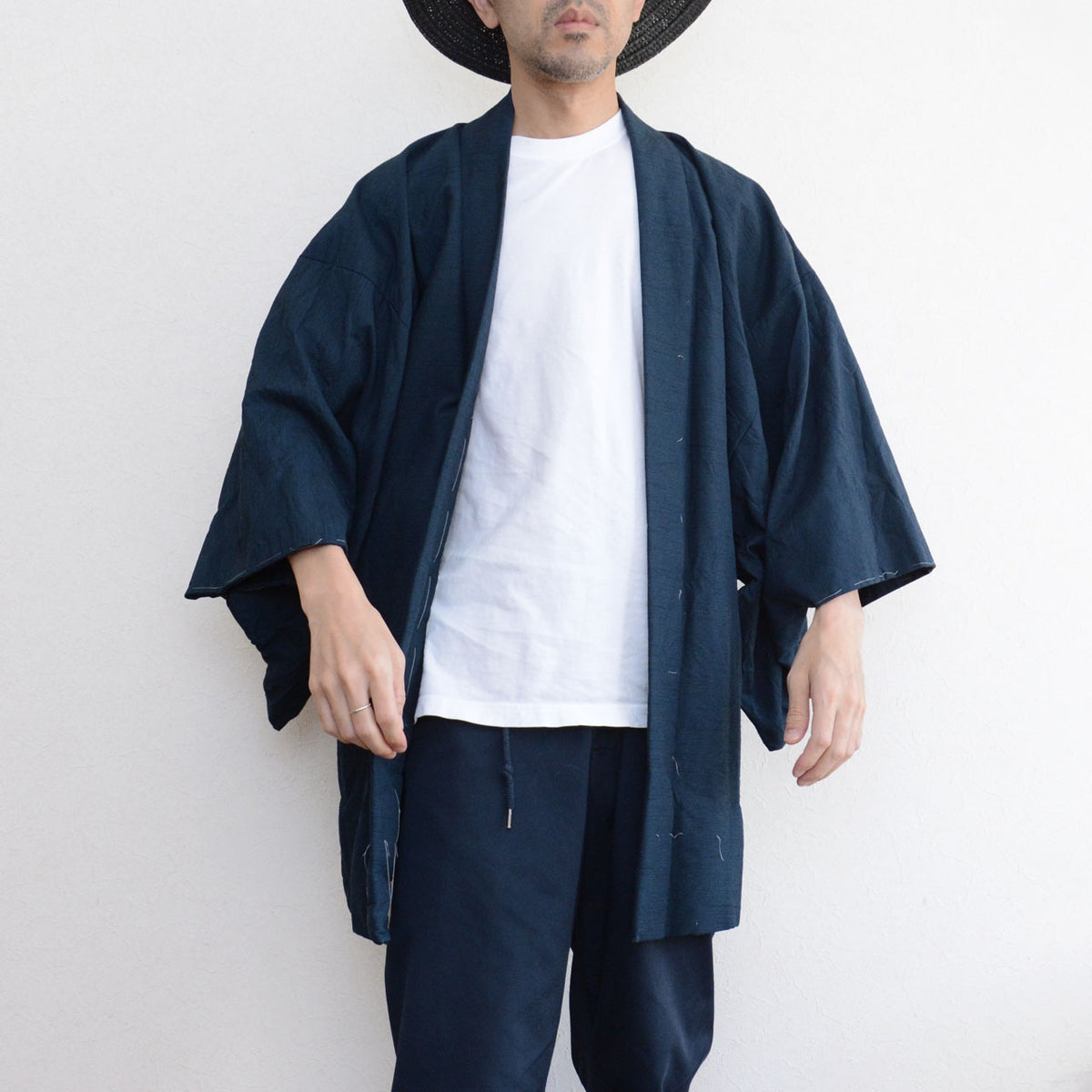 Deep blue-green Japanese vintage men's haori with remaining basting stitches, paired with a white T-shirt and dark trousers.