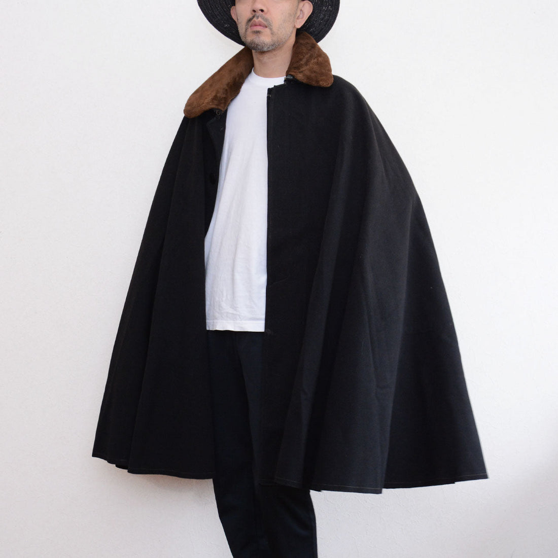 Model wearing a black Bankara mantle with a broad cape-like silhouette and brown fur collar.