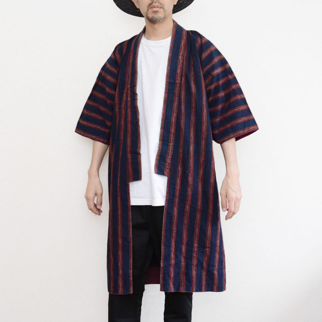 Vintage Japanese noragi jacket worn by a male model, front view — indigo-dyed cotton with bold red stripe, open-front wrap, tube sleeves, styled over white tee and black pants, Tohoku, early Showa era