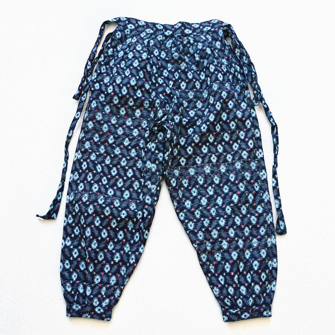 indigo kasuri cotton monpe — navy ground with light blue ikat motifs and multicolor accent threads, front view with tie waist