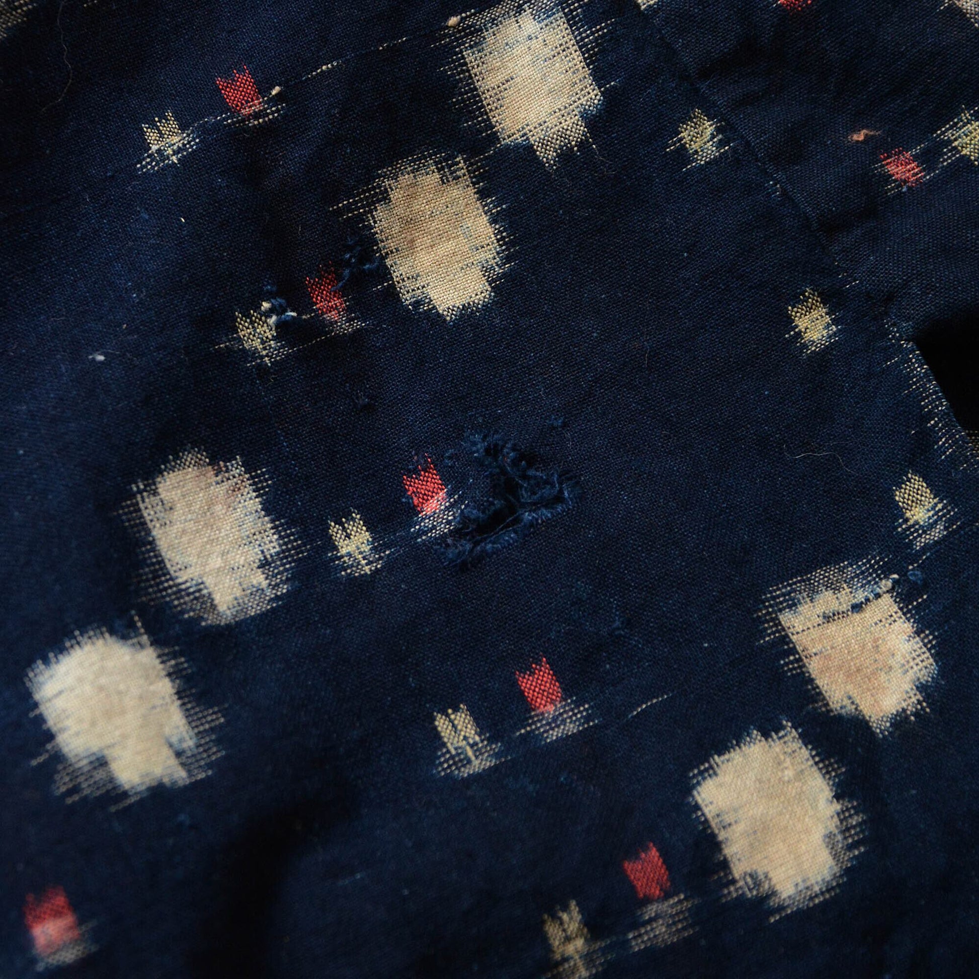 Close-up of a hole in an indigo kasuri noragi, highlighting its vintage wear and character
