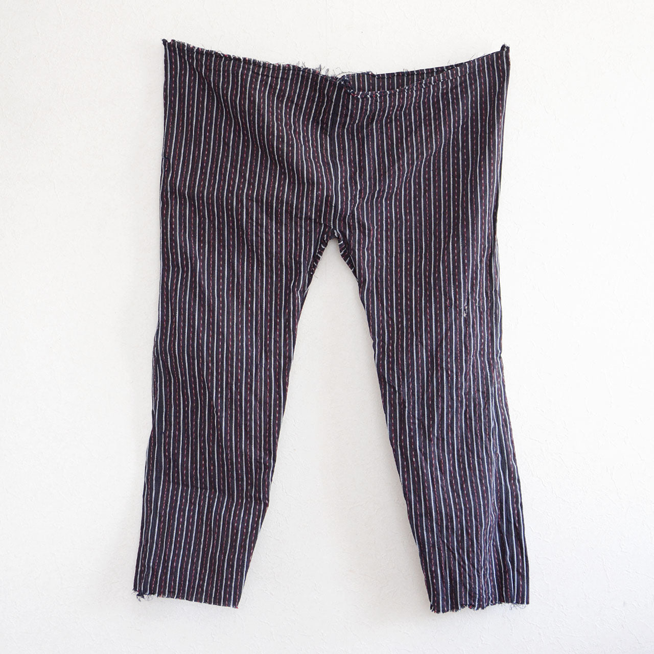 Front view of vintage Japanese monpe pants with striped cotton fabric, displayed on the wall. Showcasing the cropped waist and hem design typical of mid-Showa era workwear.