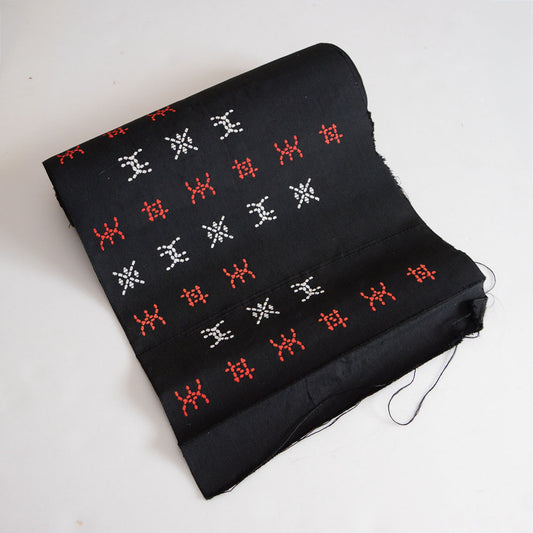 Embroidered cotton fabric in a long roll form with dark ground and contrasting stitched patterns