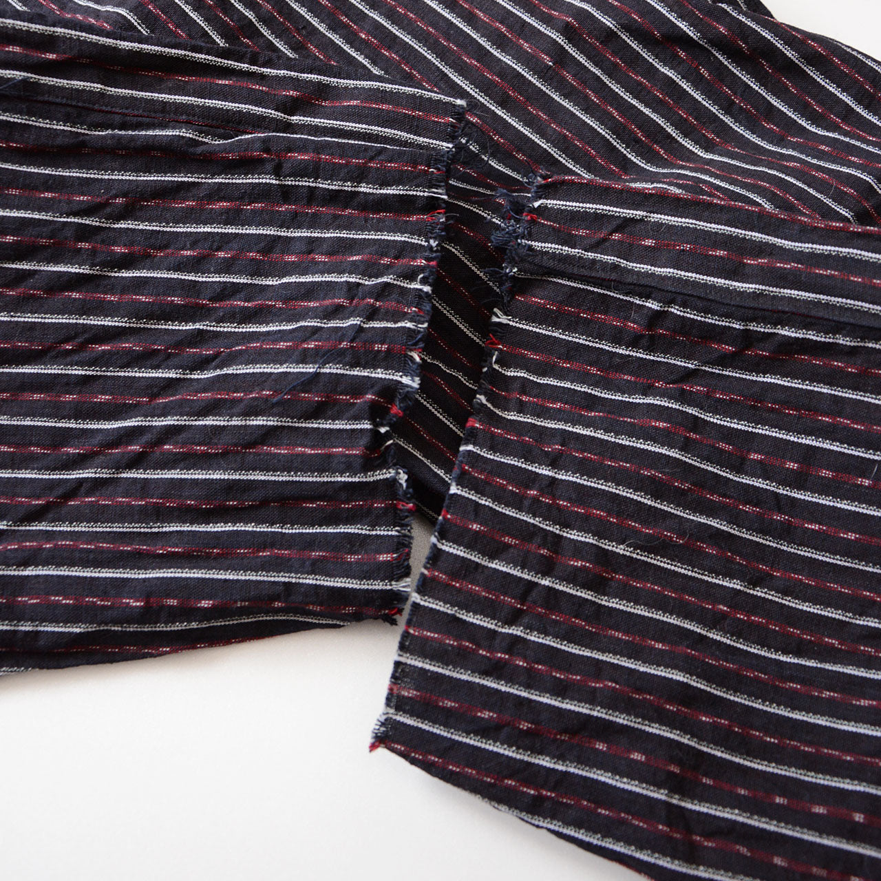 Close-up of the raw, cropped hem of vintage Japanese monpe pants made from striped cotton fabric. The unfinished hem gives a relaxed, rugged look typical of mid-Showa era style.