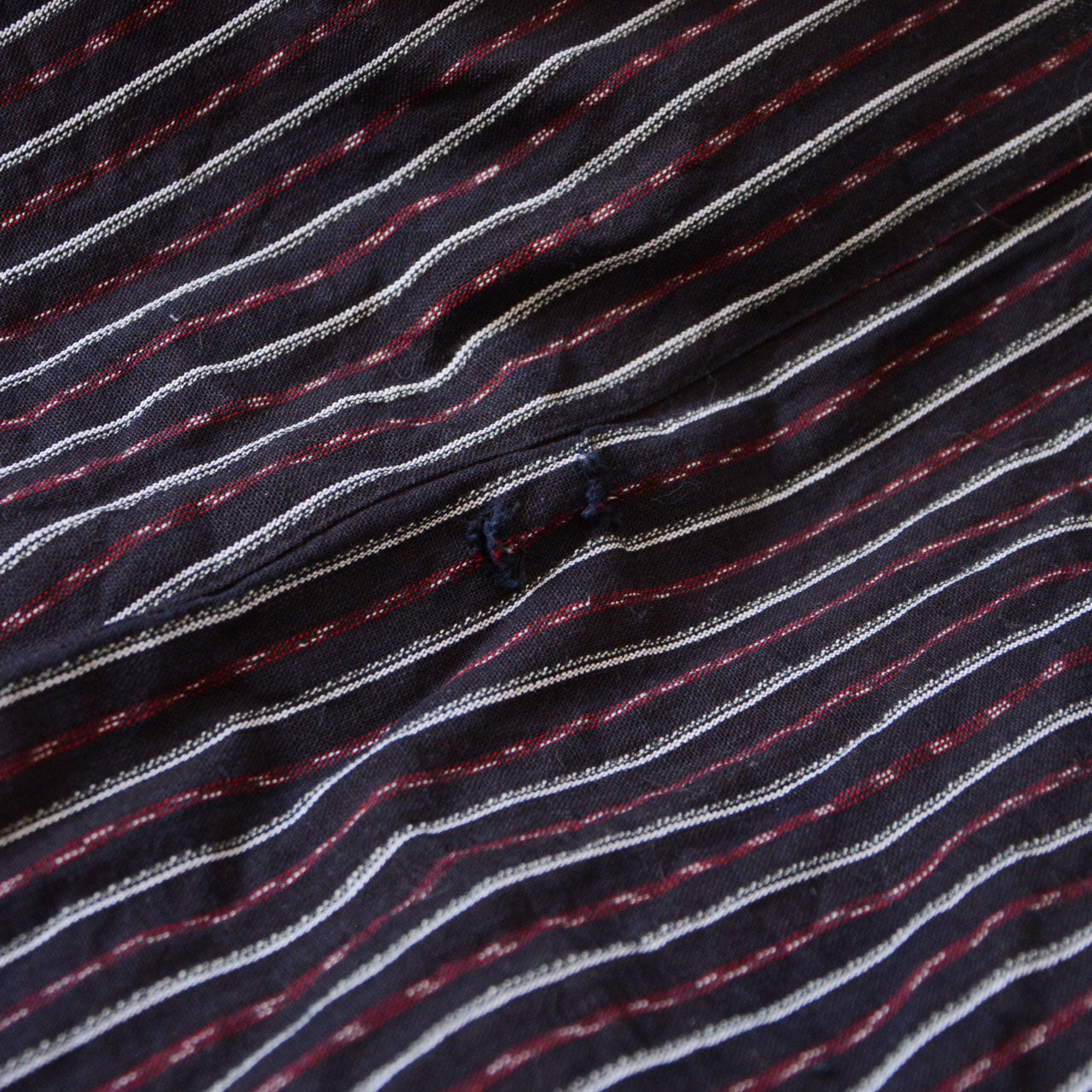 Close-up of another small hole on vintage Japanese monpe pants made from striped cotton fabric. This unique imperfection can be creatively repaired with sashiko stitching, adding character and charm to the pants.