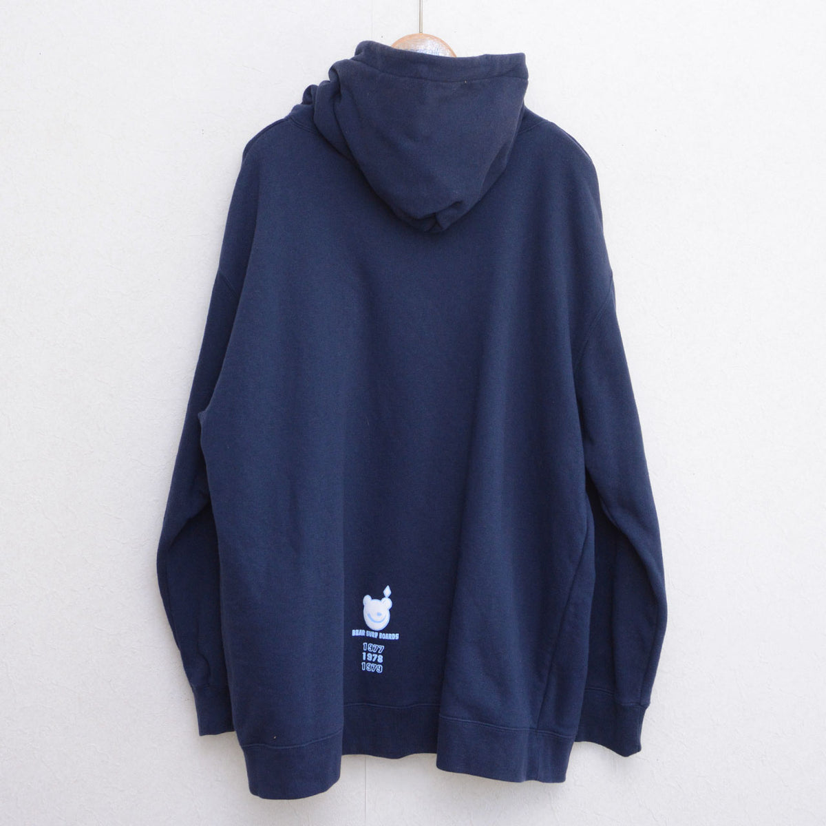 Back of navy BEAR SURFBOARDS hoodie with small bear graphic near the hem