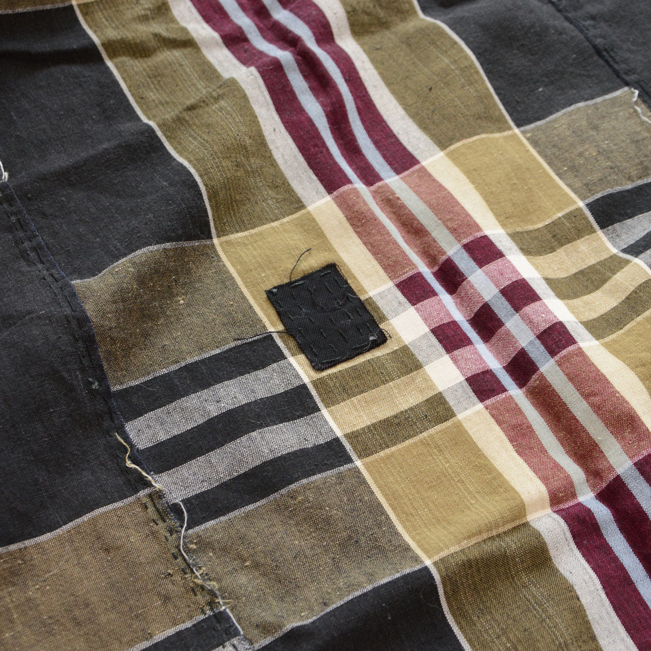Vintage Japanese boro futon-gawa fabric, plaid cotton in black, khaki, burgundy and white, close detail of small black patch repair and hand-sewn seam, Showa era