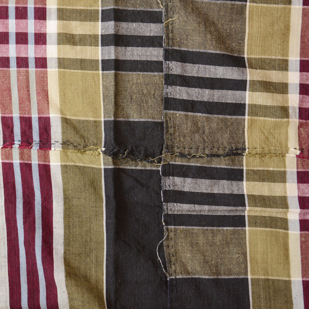 Vintage Japanese boro futon-gawa fabric, plaid cotton in black, khaki, burgundy and white, close detail of vertical panel seam with frayed and unraveling edges, Showa era