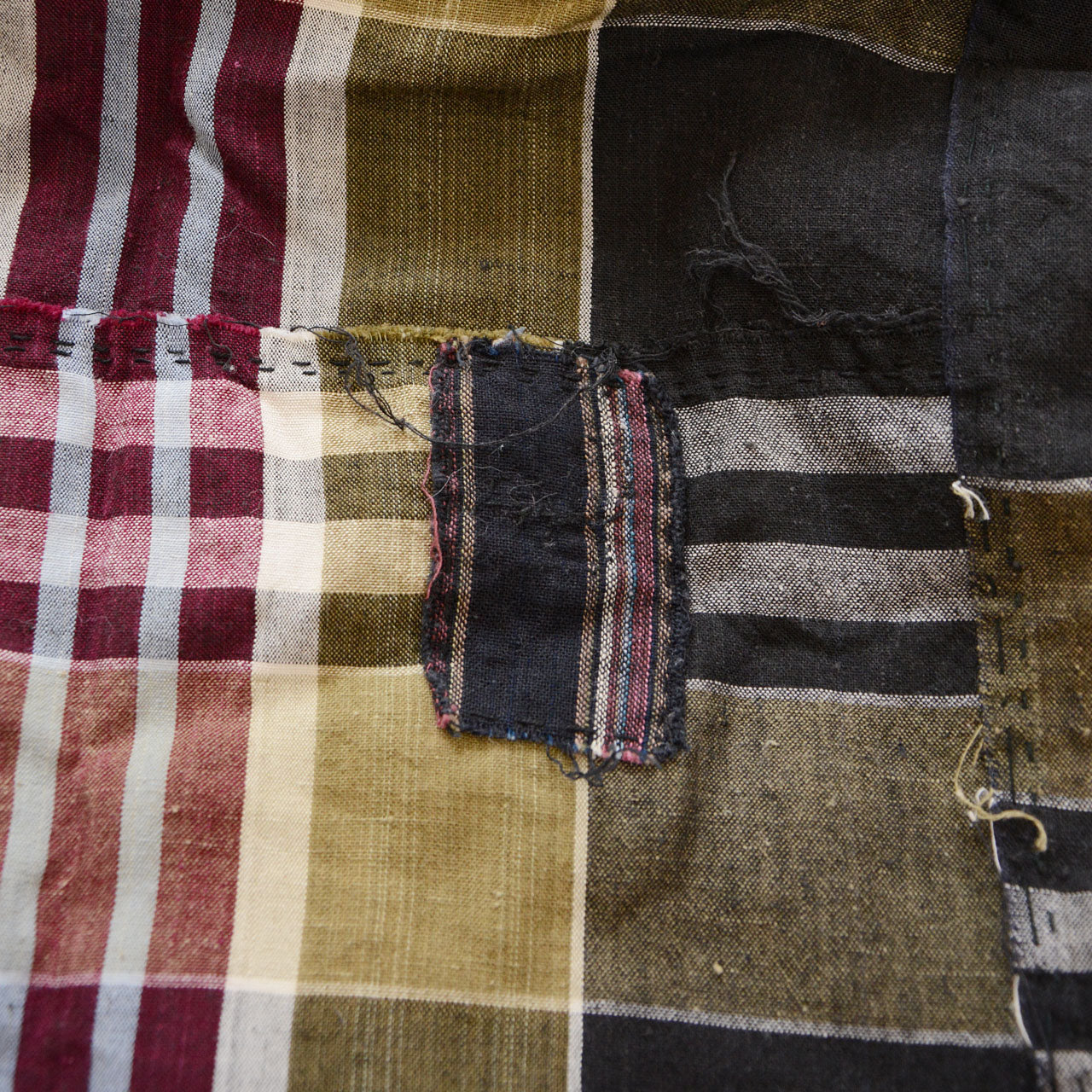 Vintage Japanese boro futon-gawa fabric, plaid cotton in black, khaki, burgundy and white, striped black patch repair with frayed edges and loose threads at seam, Showa era
