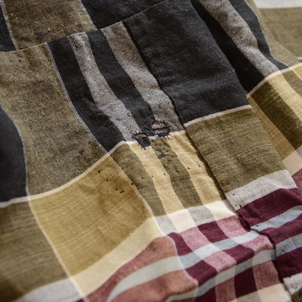Vintage Japanese boro futon-gawa fabric, plaid cotton in black, khaki, burgundy and white, close detail of panel seam intersection with small black stitch repair and aged cotton surface, Showa era