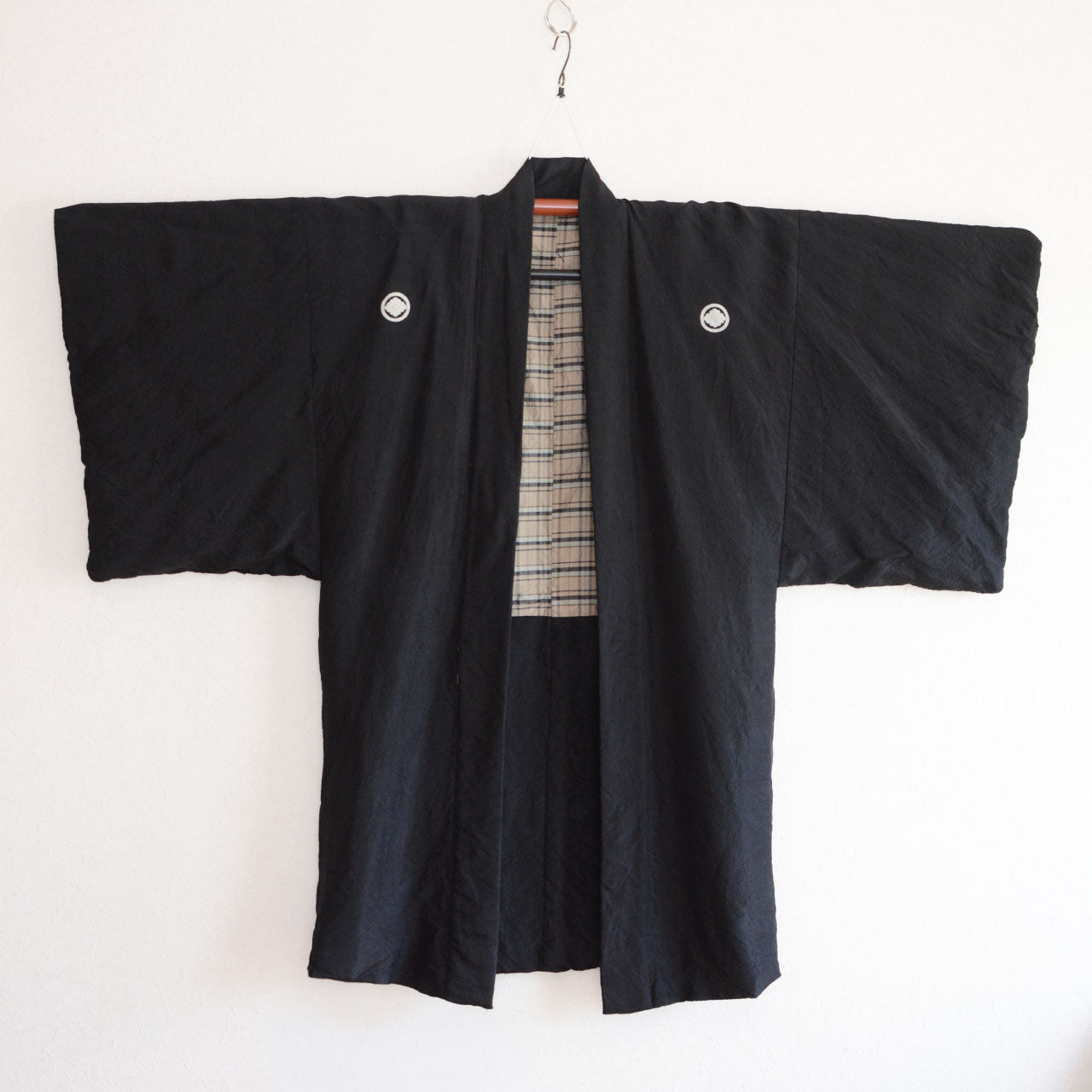 Men's black itsutsumon haori jacket on hanger, front view, two family crests on chest, checkered lining visible, Japan vintage