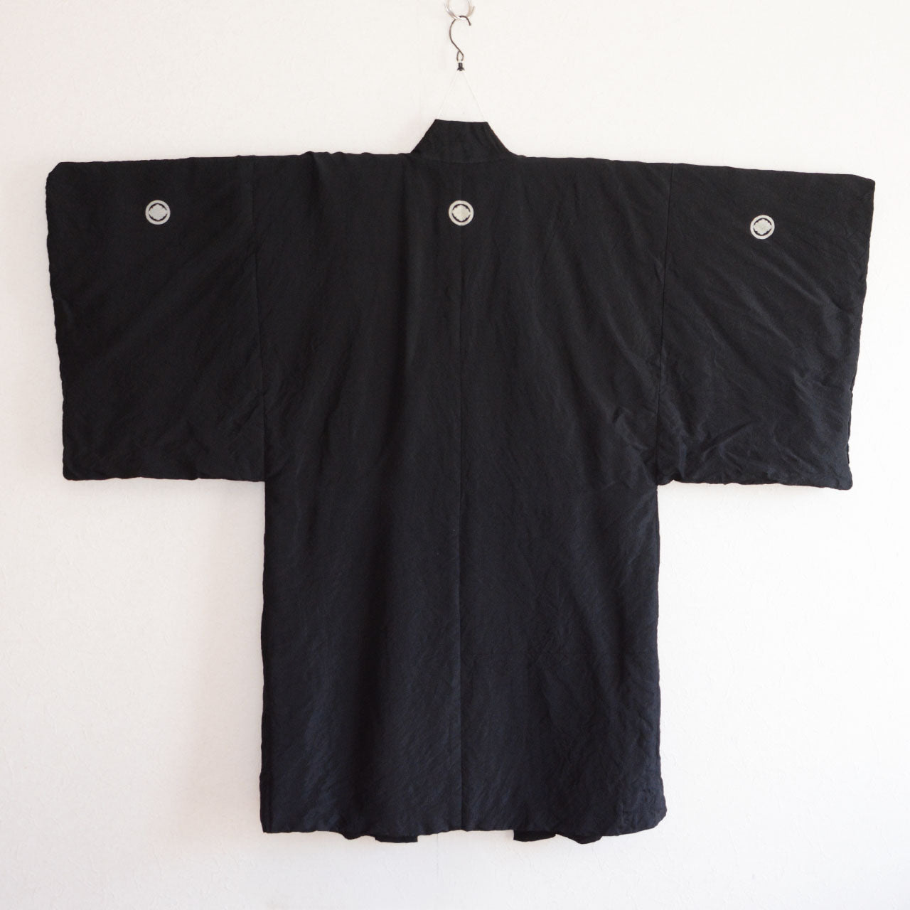 Men's black itsutsumon haori jacket on hanger, back view, three family crests across back and sleeves, Showa era Japan vintage