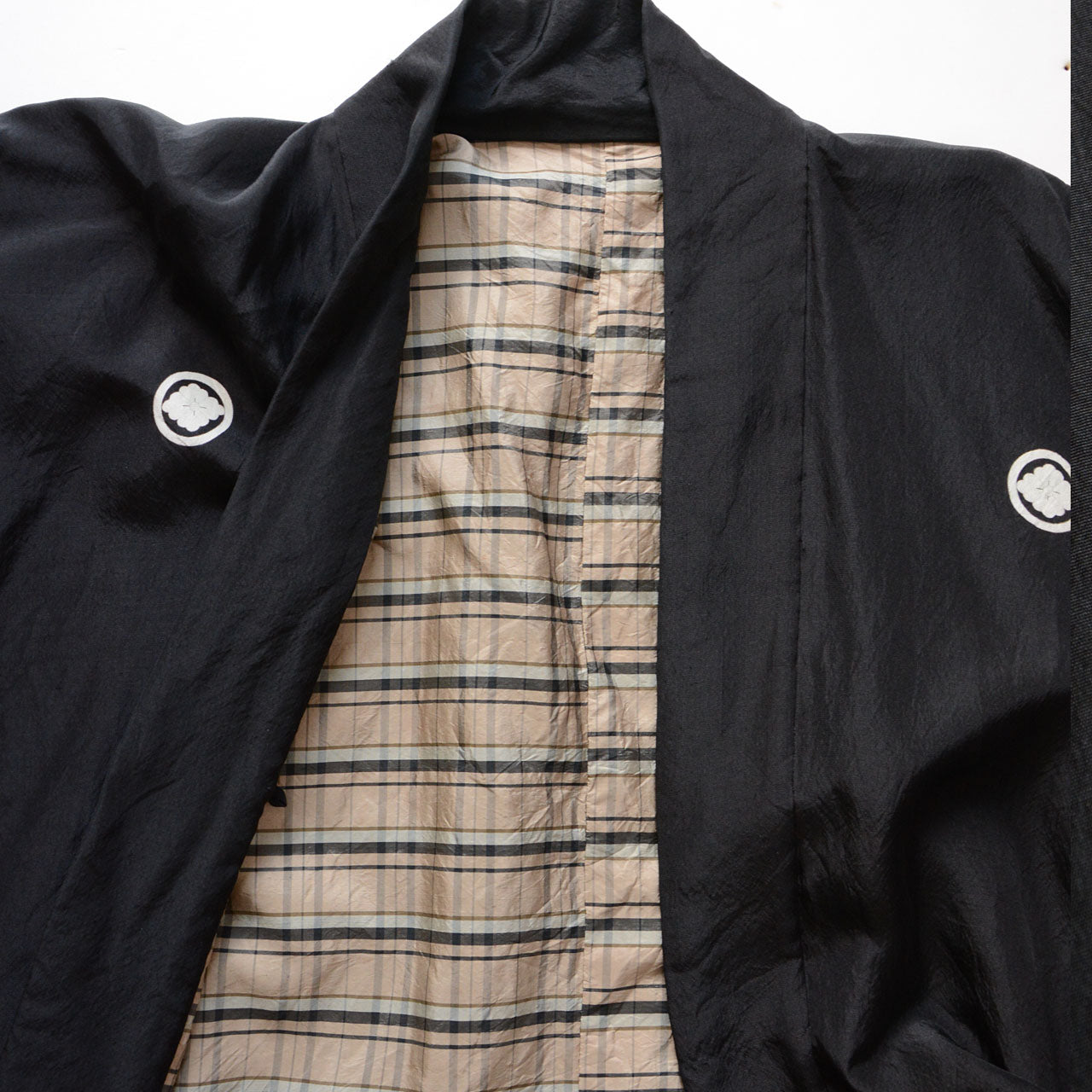 Interior view of black itsutsumon haori showing beige and black tartan checkered lining and two white mokkou family crests on chest, Japan vintage