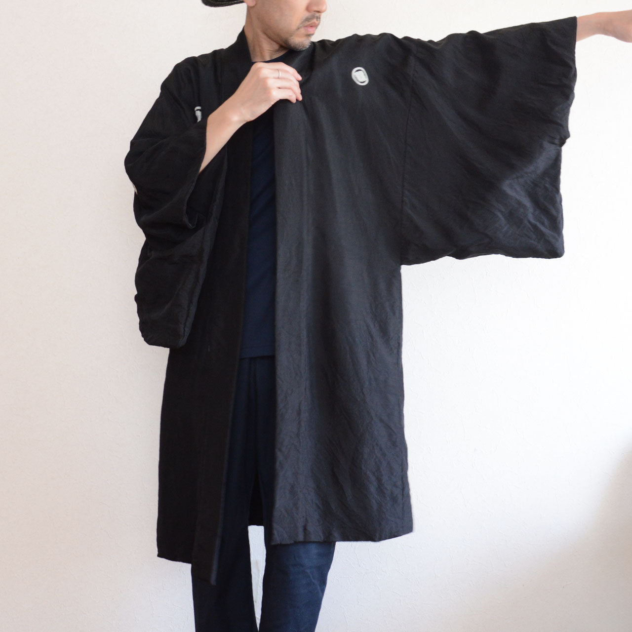Model wearing men's black itsutsumon haori jacket with arms spread wide, front view showing full sleeve width, white mokkou crest visible, model height 171 cm