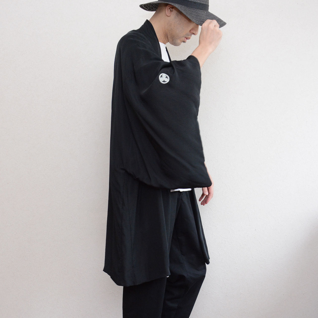 Black silk montsuki haori jacket worn over white t-shirt and black trousers, side view showing Maru ni Mitsu Kashiwa family crest on sleeve, wide silhouette, Japan vintage 1970s–80s