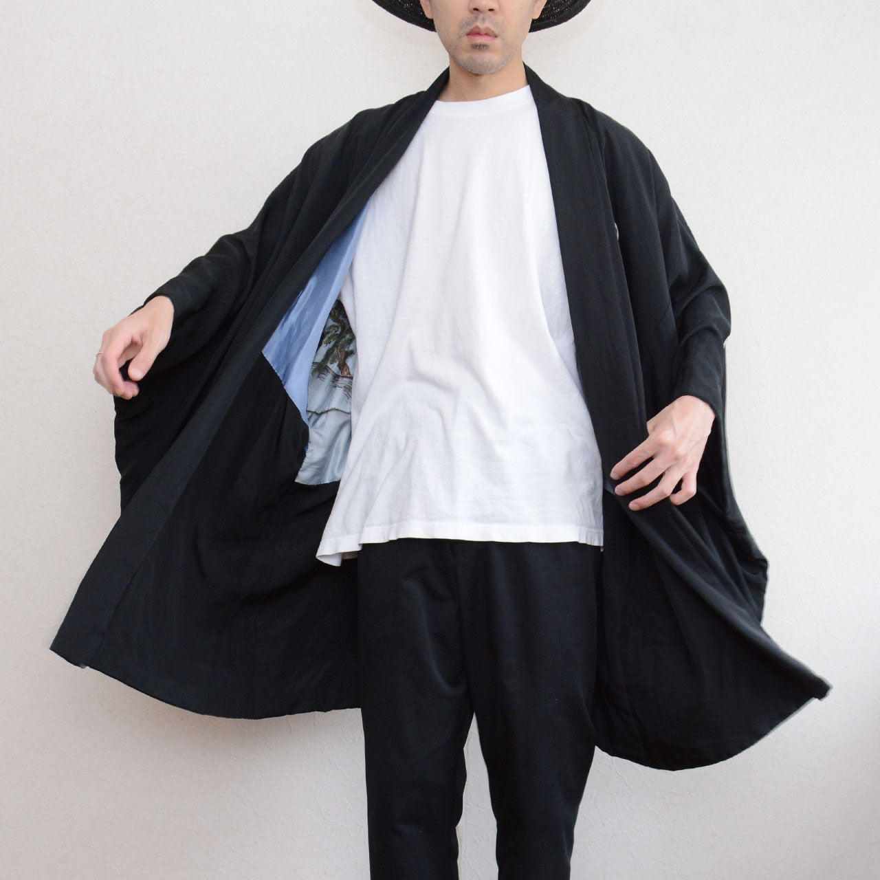 Black silk montsuki haori jacket worn open over white t-shirt and black trousers, front view showing pale blue hand-painted landscape lining (haura) visible at center opening, Japan vintage 1970s–80s