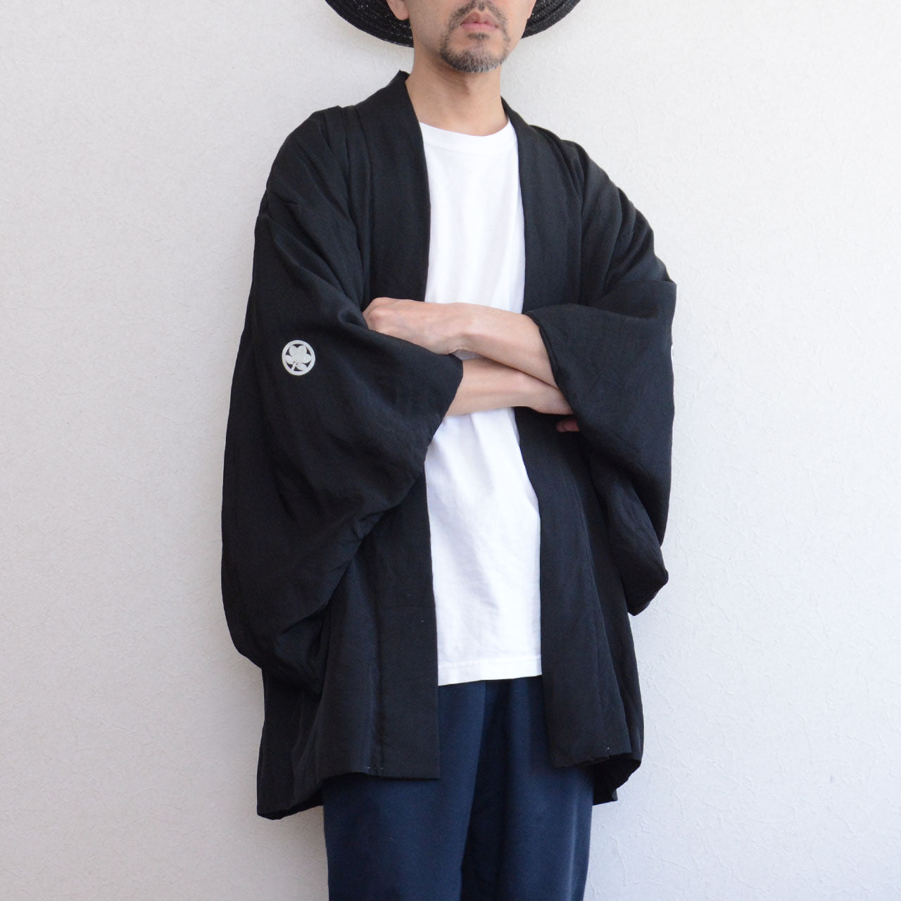 Model wearing men's black silk itsutsumon haori with arms crossed, front view