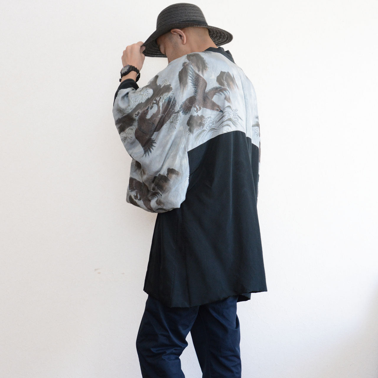 Model wearing black silk haori from behind, lining visible through open sleeves, styled with navy pants and wide-brim hat, model height 171 cm