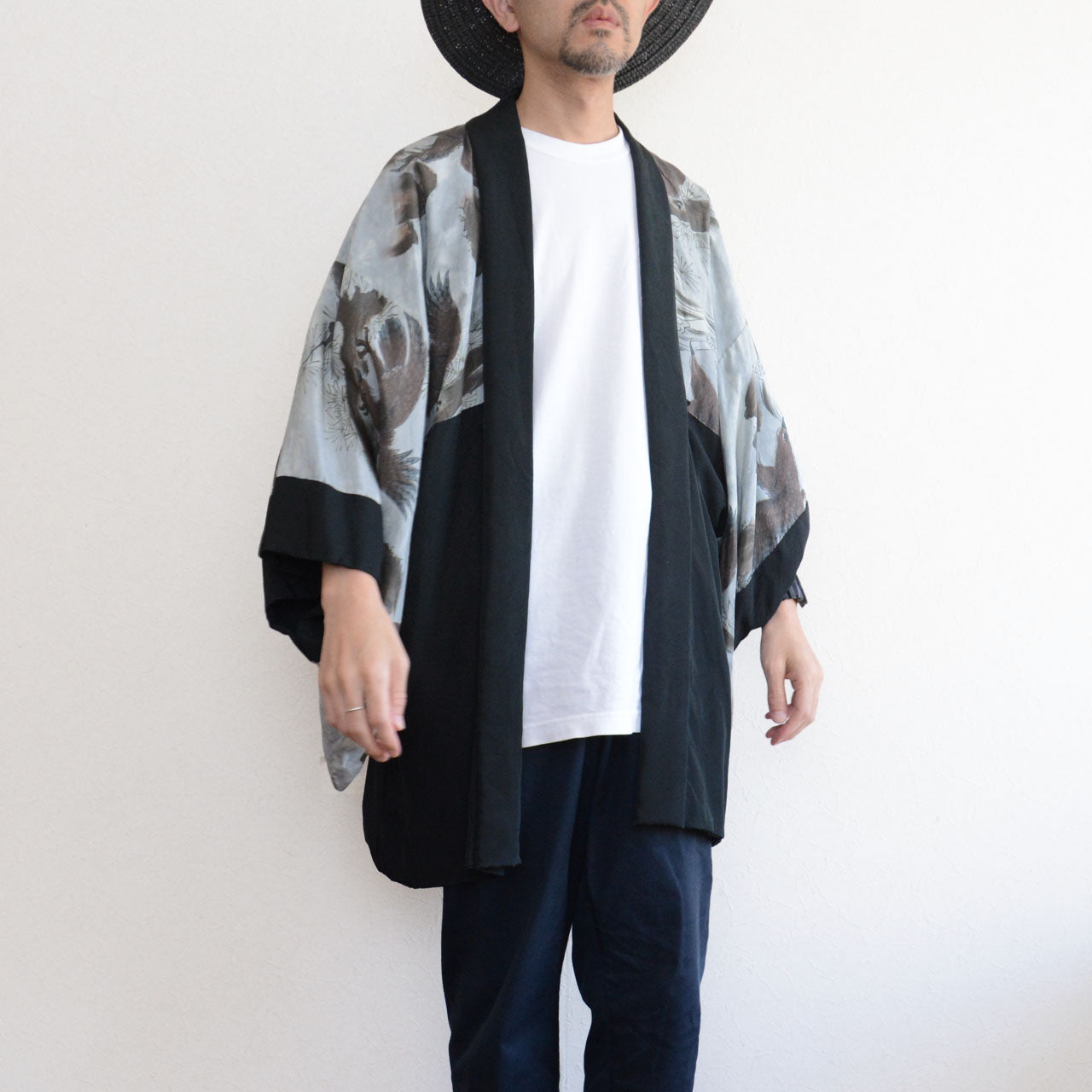 Model wearing black silk haori jacket, front view, white tee underneath, navy pants, wide-brim hat, kamon visible at chest, model height 171 cm