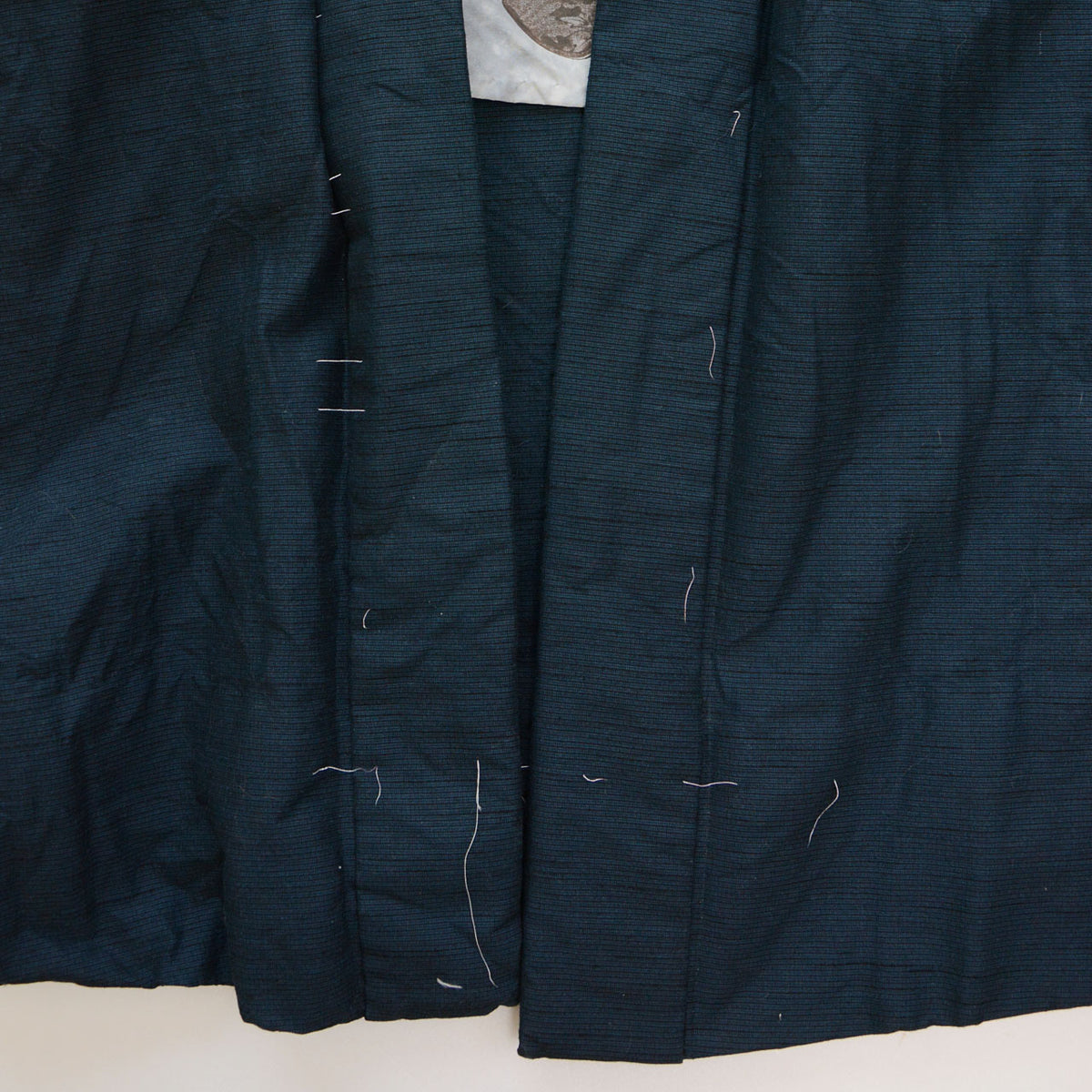 Deep blue-green haori collar and front panels with remaining white basting stitches.