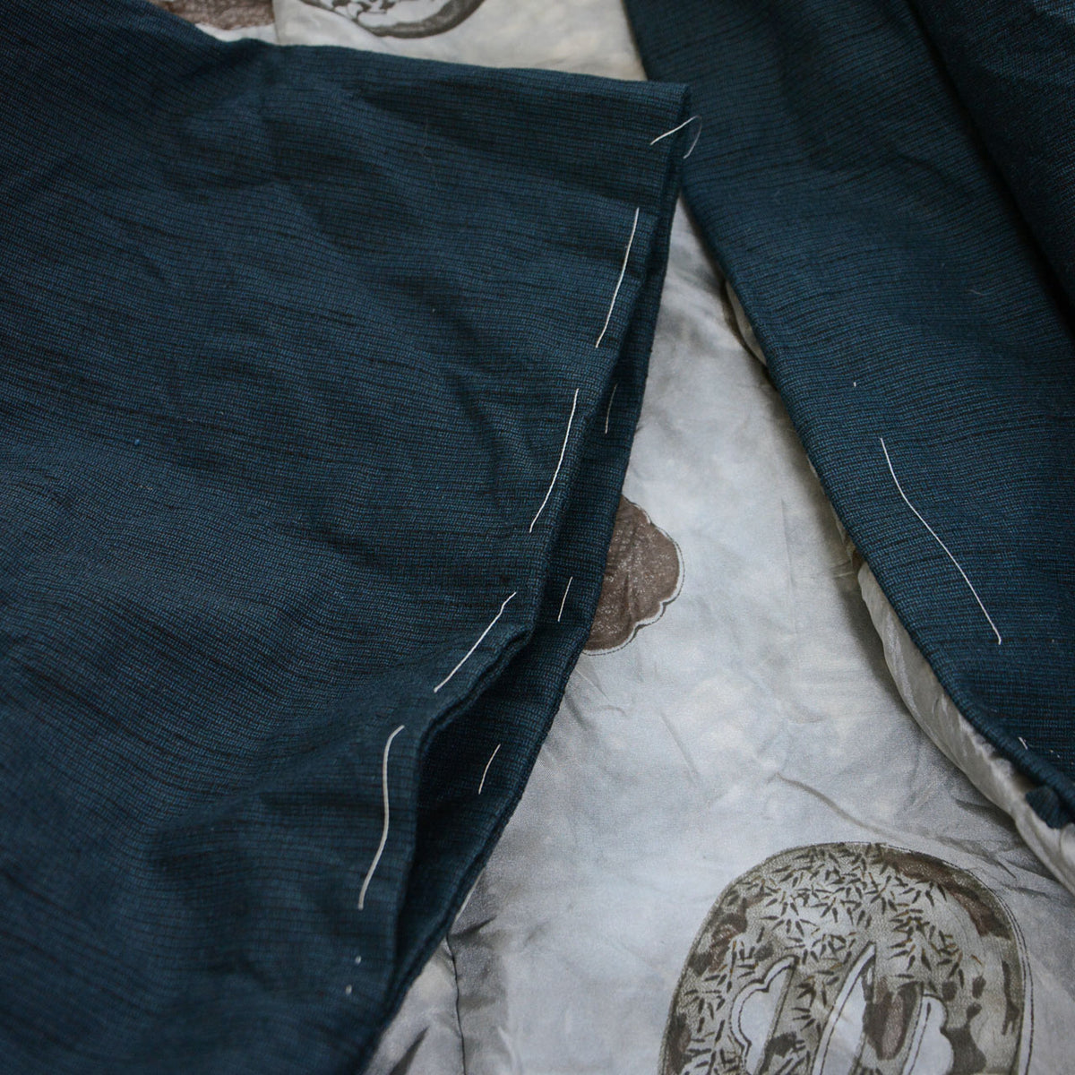 Deep blue-green haori sleeve opening with remaining white basting stitches and a light-colored patterned lining.