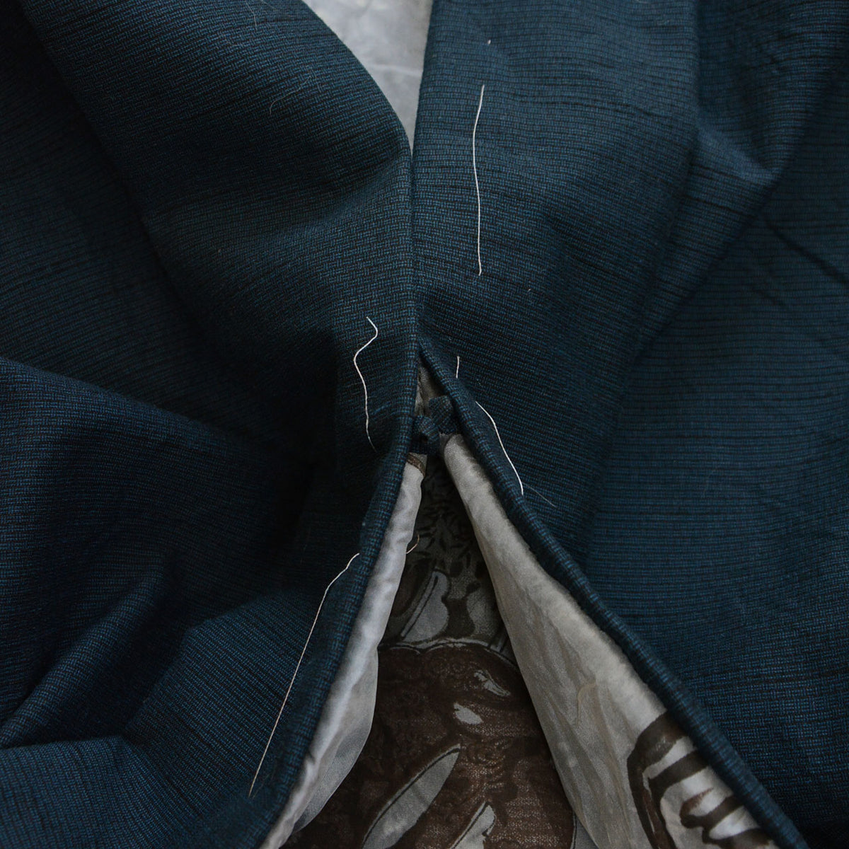 Fabric loop for attaching a haori tie, with deep blue-green fabric and remaining white basting stitches.