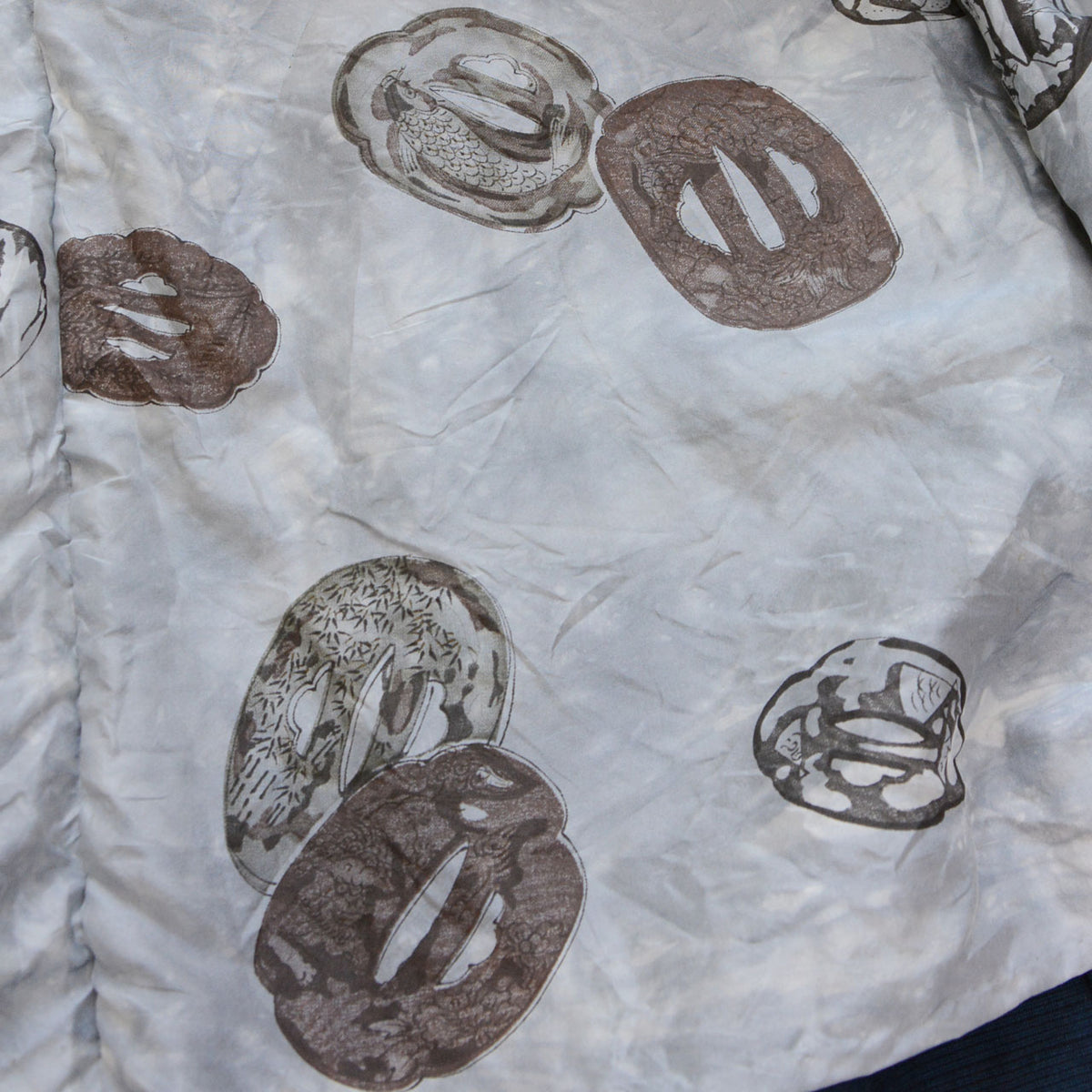 Tsuba sword-guard motifs in varied shapes and decorative designs on a light gray Japanese haori lining.