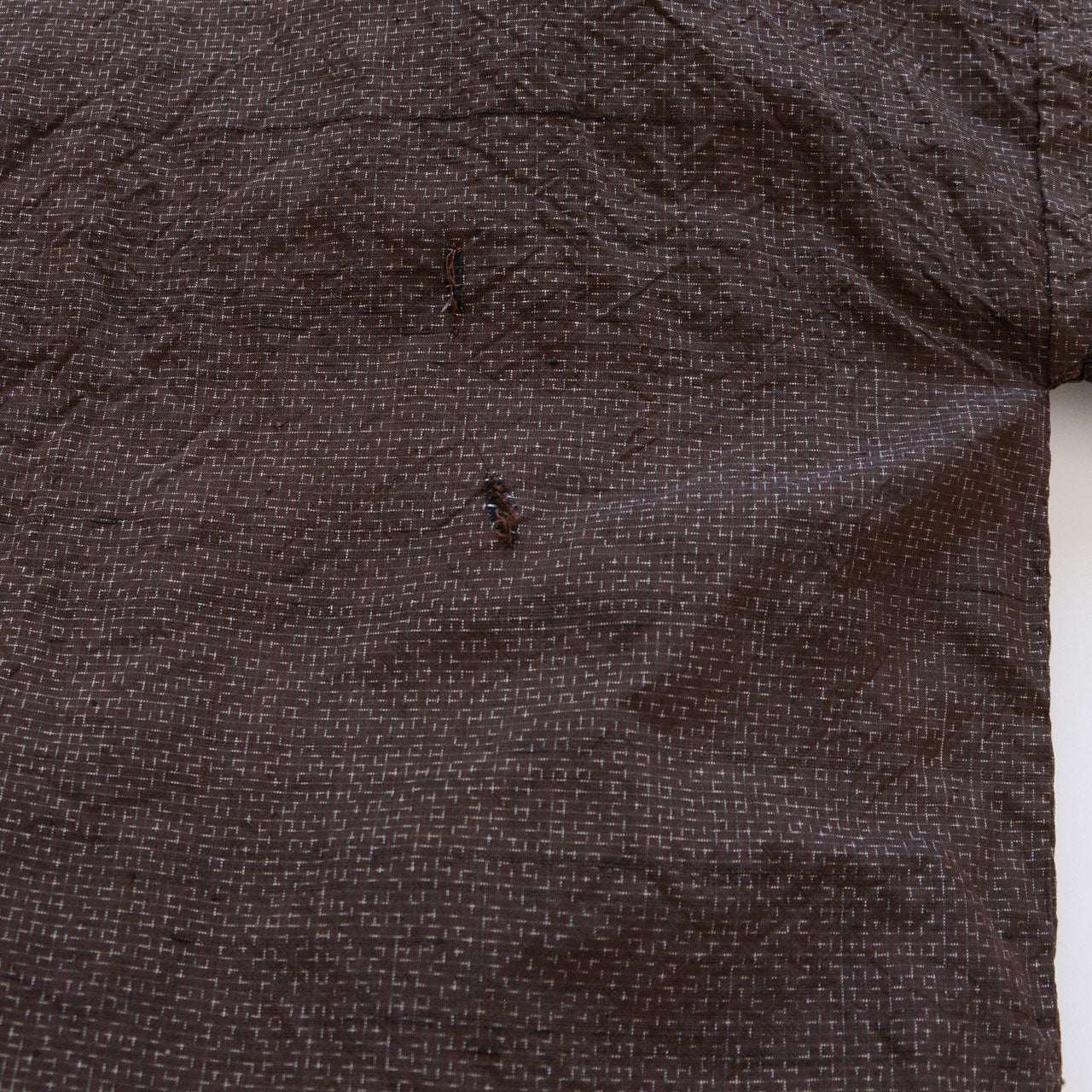 Close-up of fabric damage — hole and thread slippage on dark brown woven haori jacket, vintage condition