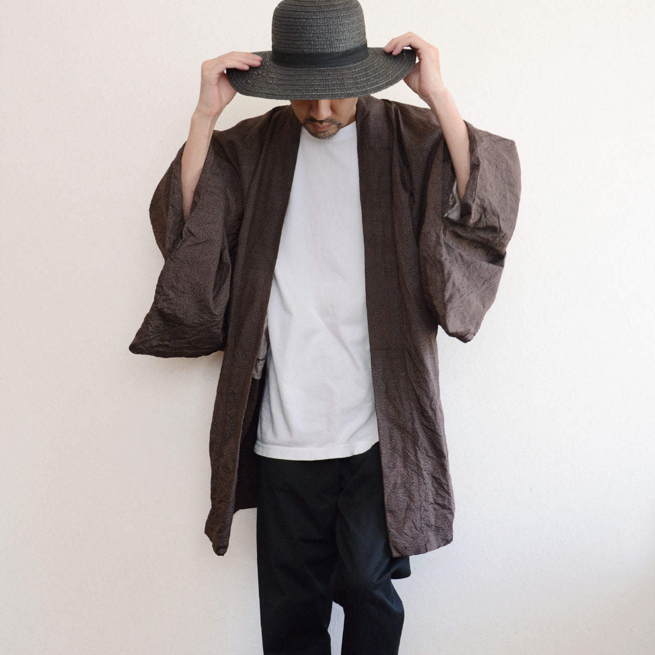 Man wearing a dark brown vintage Japanese haori jacket over a white t-shirt and black trousers with a straw hat — open front, wide sleeves, 1970s–1980s Japan