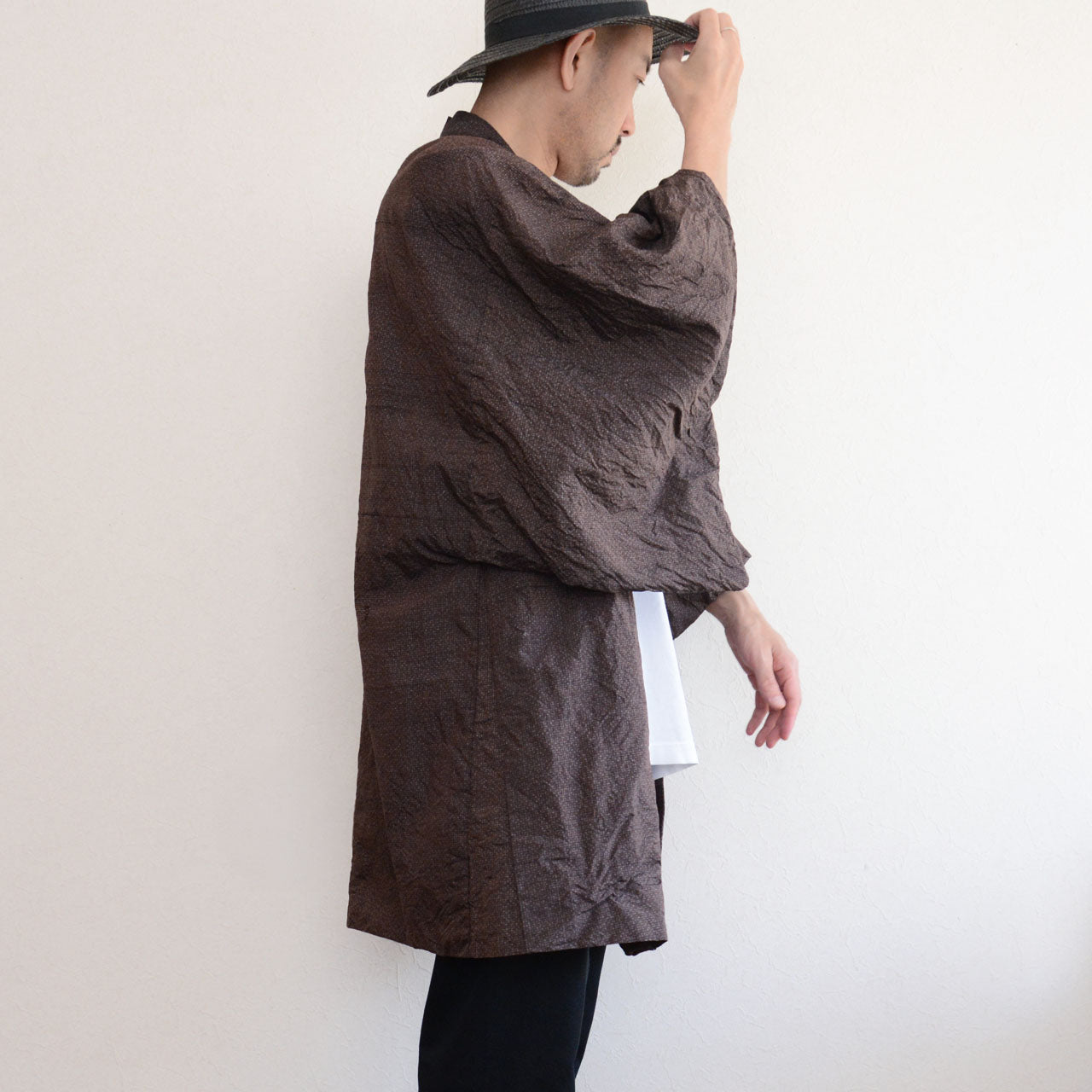 Man wearing a dark brown vintage Japanese haori jacket — side view, open front drape, layered over white t-shirt and black trousers, straw hat