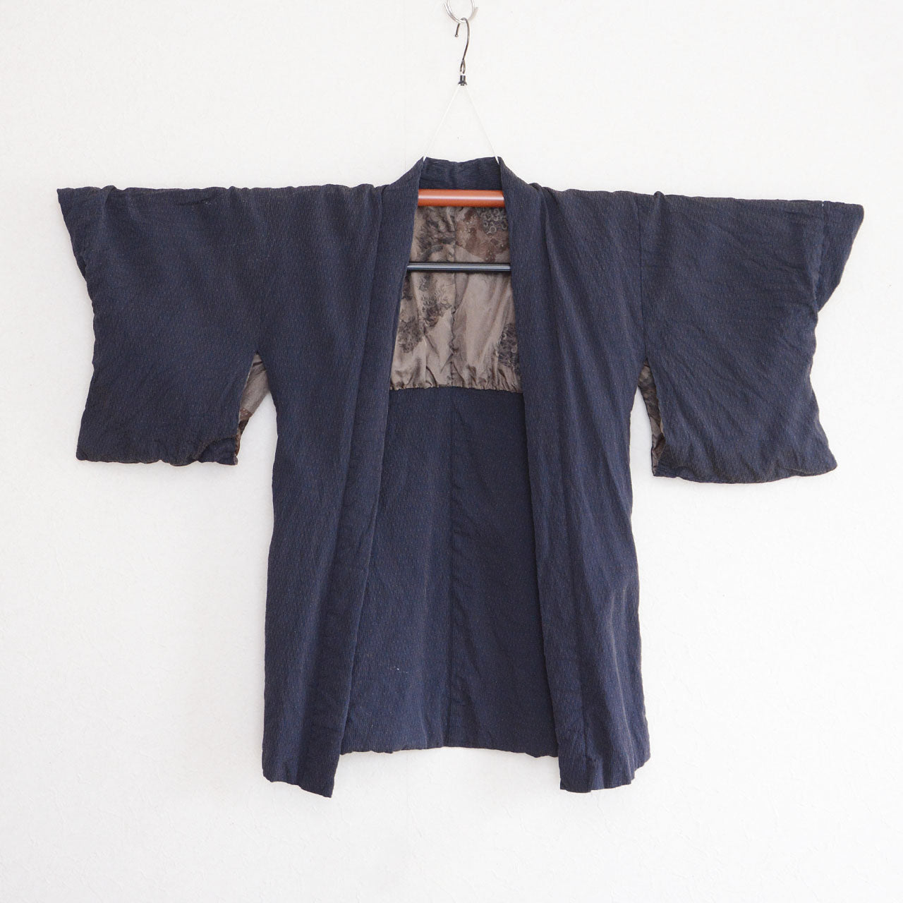 Front view of a deep navy Japanese vintage haori kimono jacket on a kimono hanger, with scenic lining visible