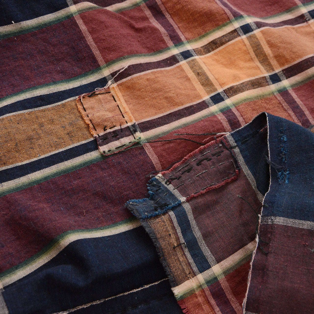 Boro patch repair detail on vintage Japanese futon cover — layered cotton mending cloth hand-stitched onto aged plaid ground fabric
