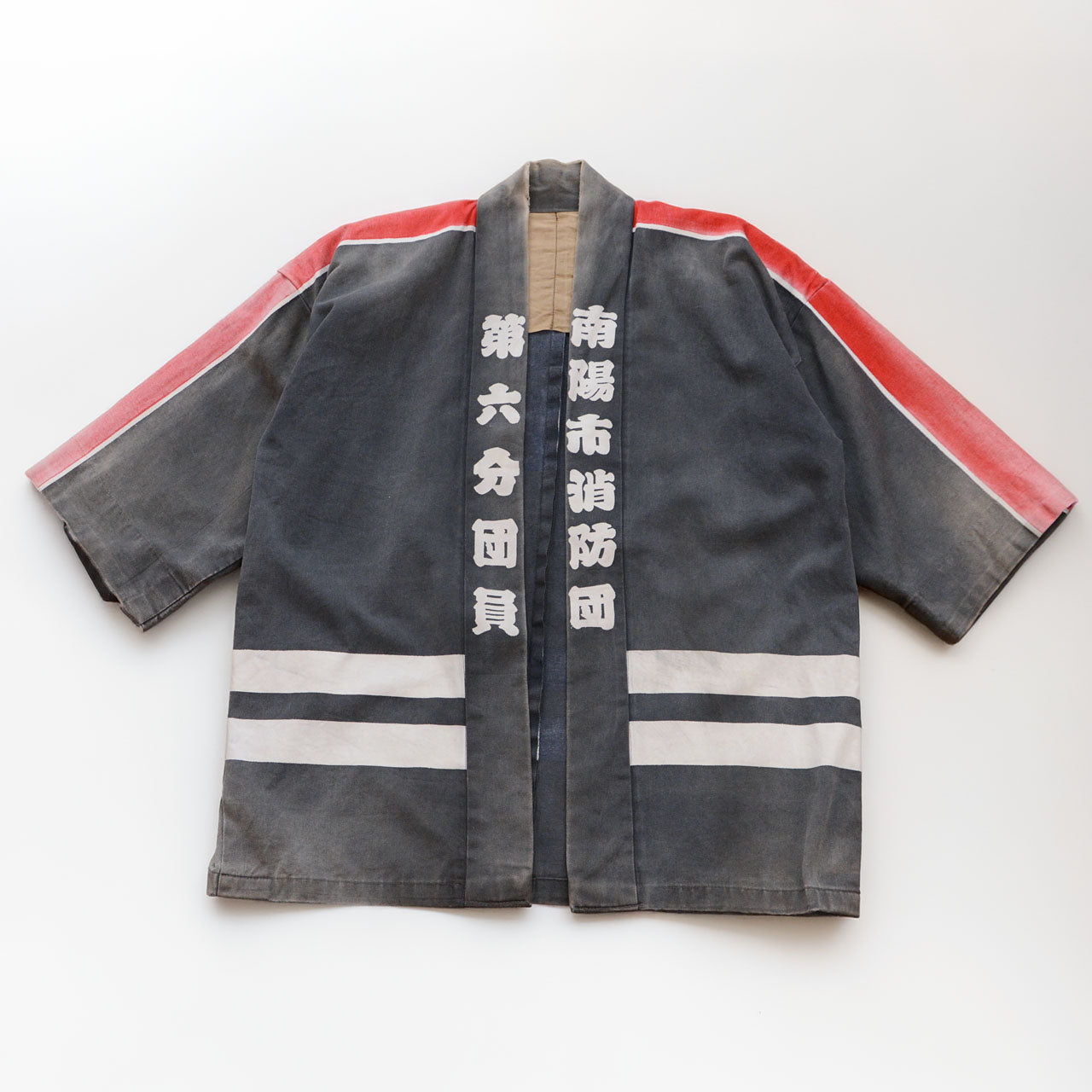 Front of a faded charcoal-gray cotton Japanese firefighter happi jacket with red and white shoulder stripes, white collar lettering, and two white horizontal hem stripes