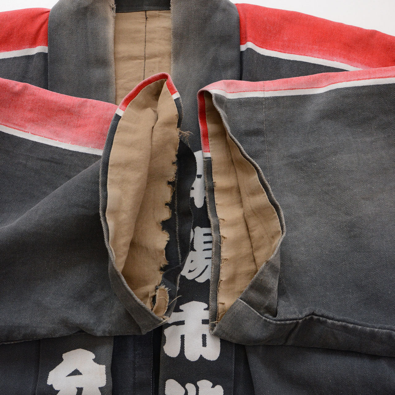 Underarm opening with missing stitching and a large tear revealing the beige inner fabric of a faded charcoal-gray cotton Japanese firefighter happi jacket