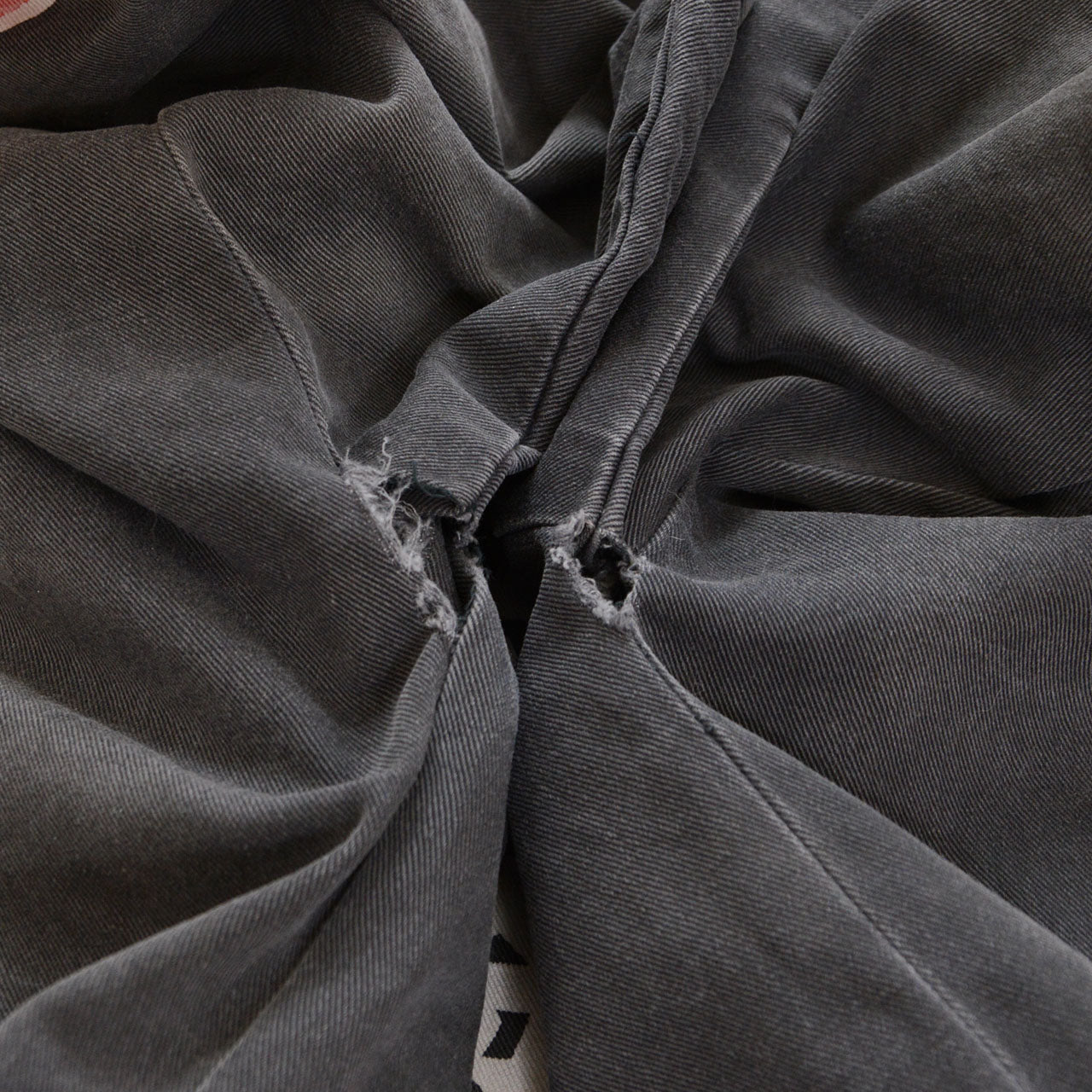 Damaged seam opening and frayed fabric on a faded charcoal-gray cotton Japanese firefighter happi jacket