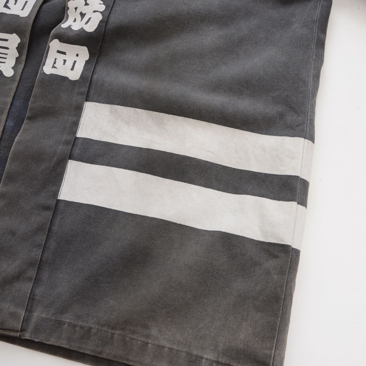 Close-up of two white horizontal stripes near the hem of a faded charcoal-gray cotton Japanese firefighter happi jacket
