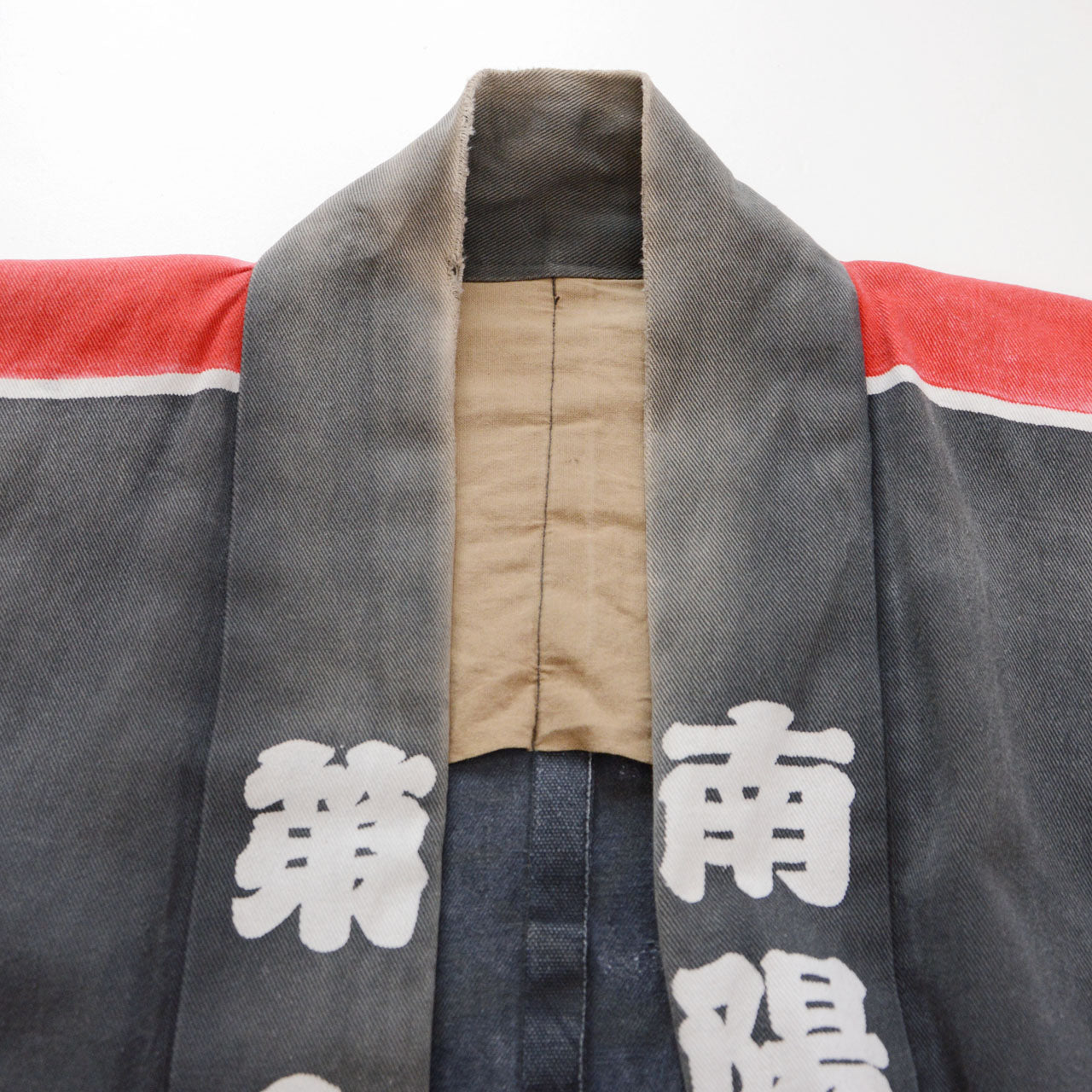 Worn collar, beige inner fabric, and red and white shoulder stripes on a faded charcoal-gray cotton Japanese firefighter happi jacket