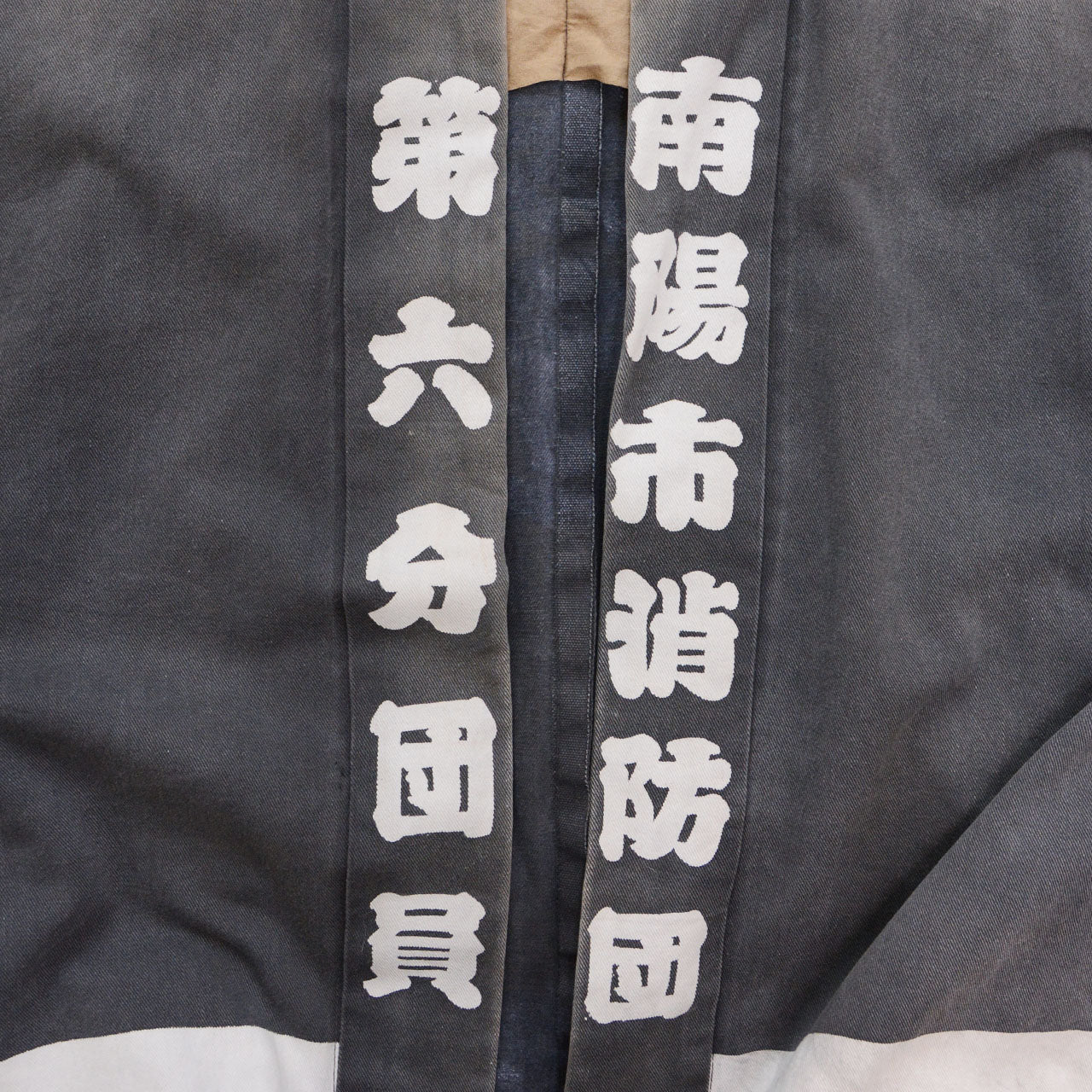 White kanji lettering on the front panels of a faded charcoal-gray cotton Japanese firefighter happi jacket