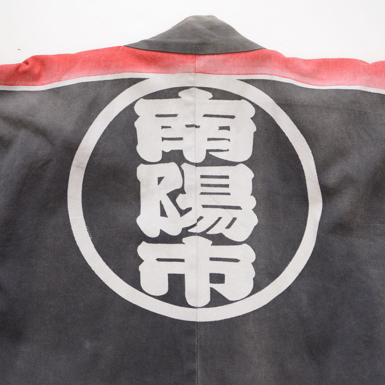 Large circular kanji crest on the back of a faded charcoal-gray cotton Japanese firefighter happi jacket