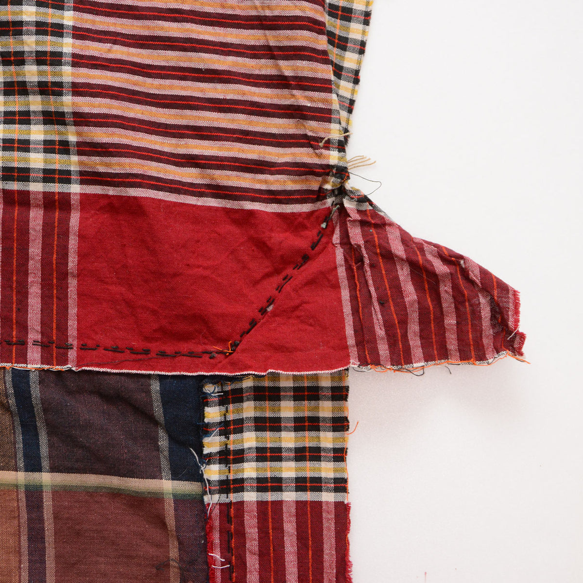 Red striped cotton fabric with hand stitching, patch repair, loose threads, and joined checkered panels