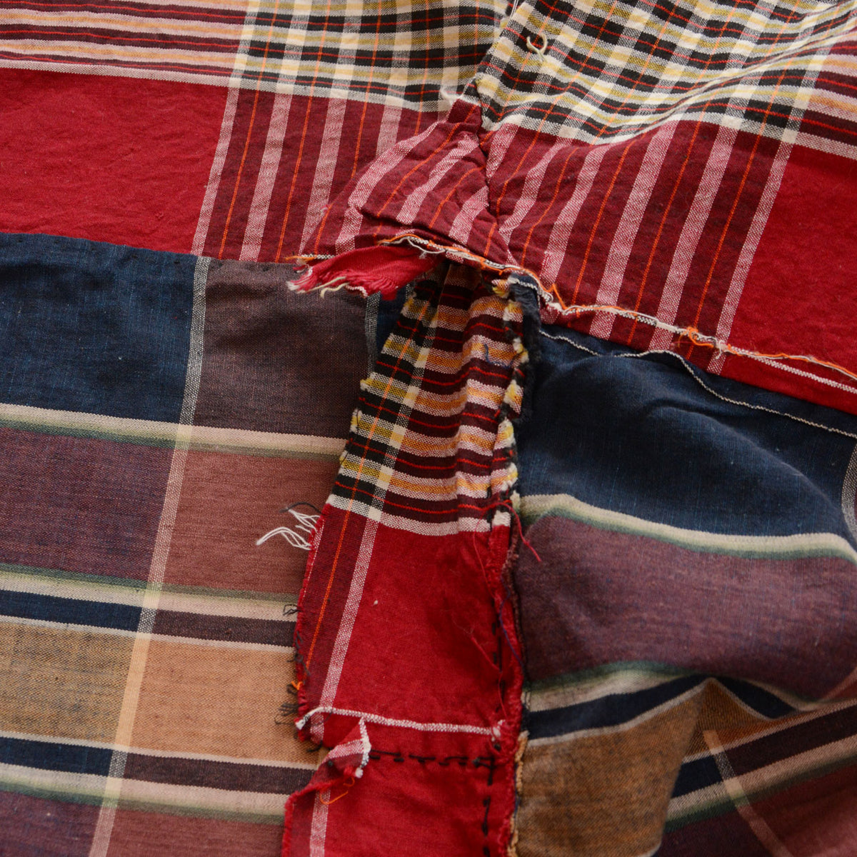 Red striped, multicolored plaid, and indigo cotton fabric with a frayed joined seam and hand stitching