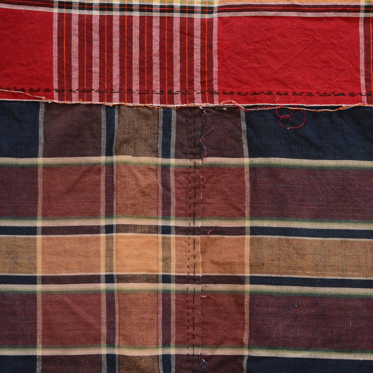 Red striped and indigo checkered cotton fabric with visible repair stitching and frayed edges