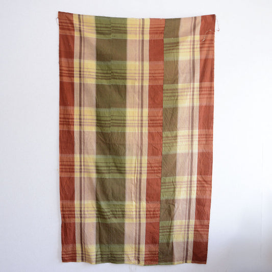 Japanese vintage cotton fabric, multicolor plaid pattern in rust red, olive green, cream, and mauve, unstitched from a Showa-era futon, needle holes and residual threads visible along seam edges