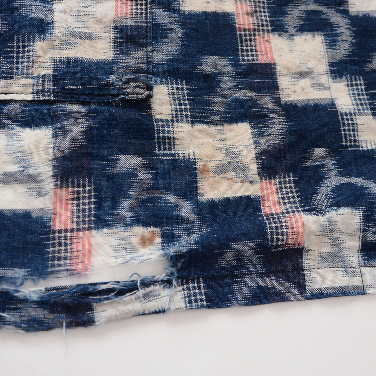Japanese vintage indigo kasuri cotton fabric with brown stains on white motifs and tears and fraying near the fabric edge