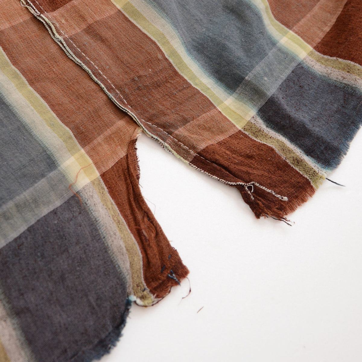 Japanese vintage checkered cotton fabric with a large tear, exposed white background, frayed fibers, and worn brown and blue-gray sections
