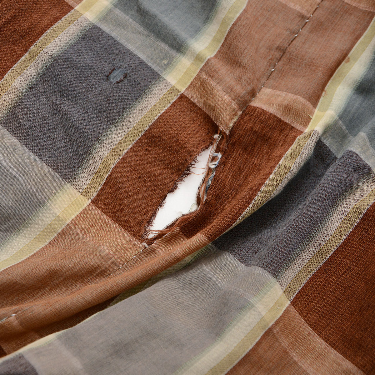 Japanese vintage checkered cotton fabric with a hole caused by missing stitches and a dark blue plaid repair patch