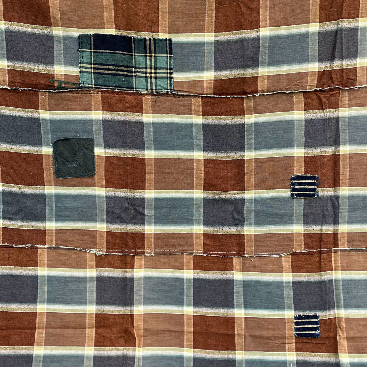 Japanese vintage cotton fabric with a brown, blue-gray, and cream checkered pattern, teal and dark repair patches, and joined seams