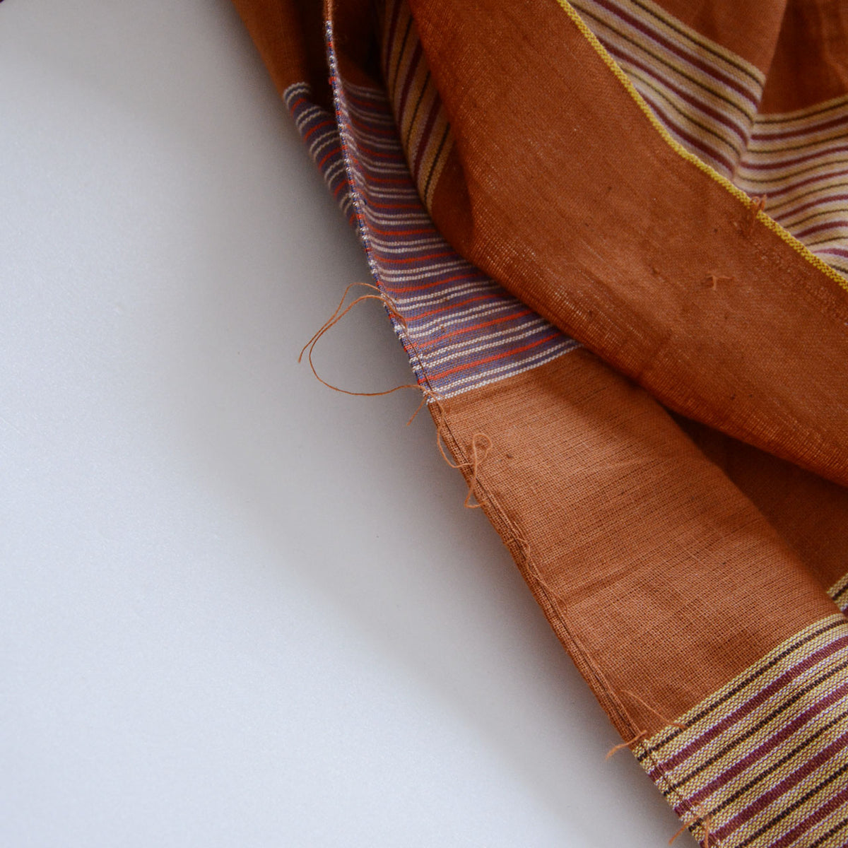 Loose threads at the edge of a brown cotton furoshiki with fine stripes